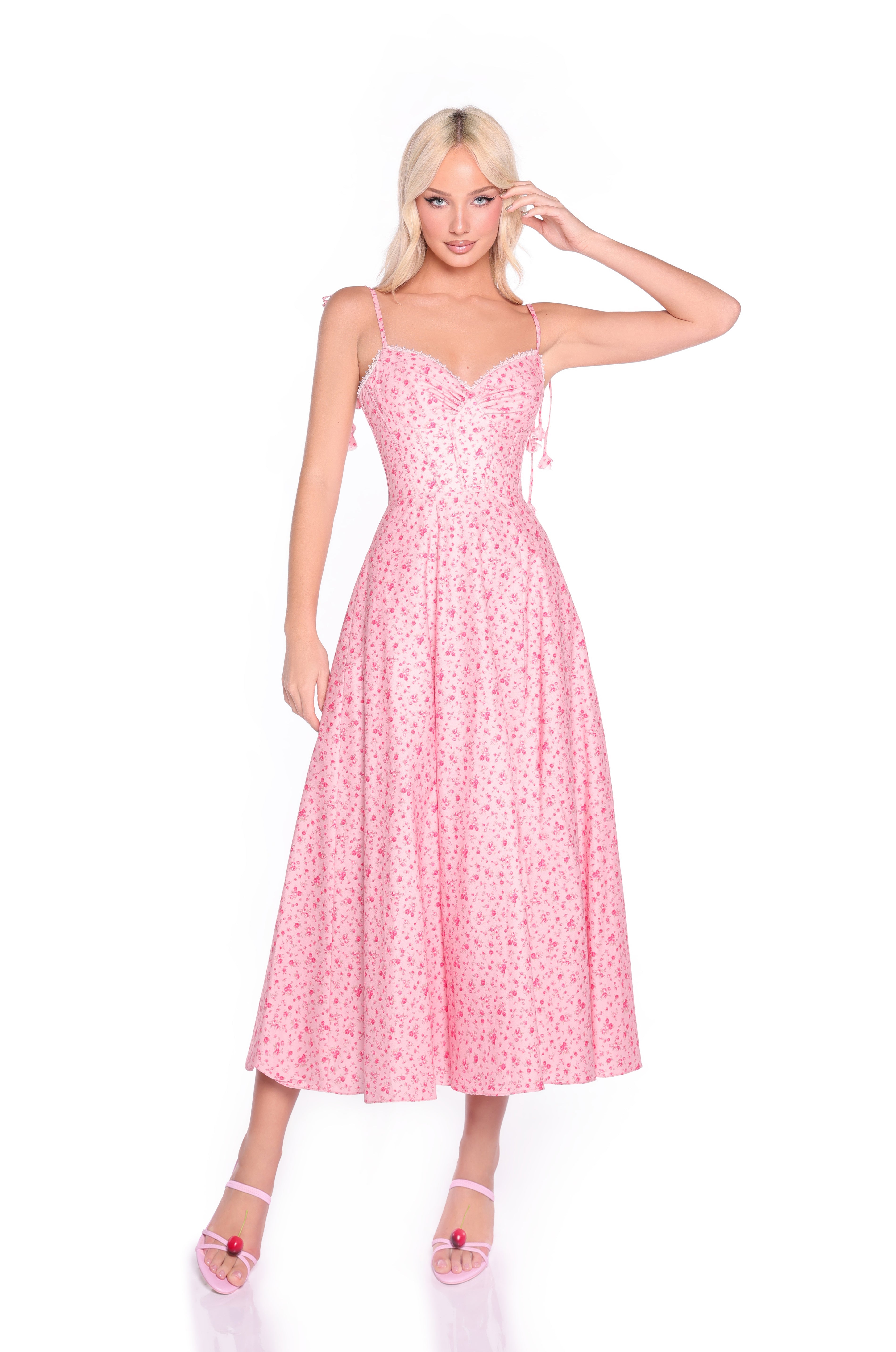 A woman models the Casual Midi Pink Floral Dress: Aria, featuring a corset bodice and flared skirt, paired with pink high-heeled sandals against a white background.